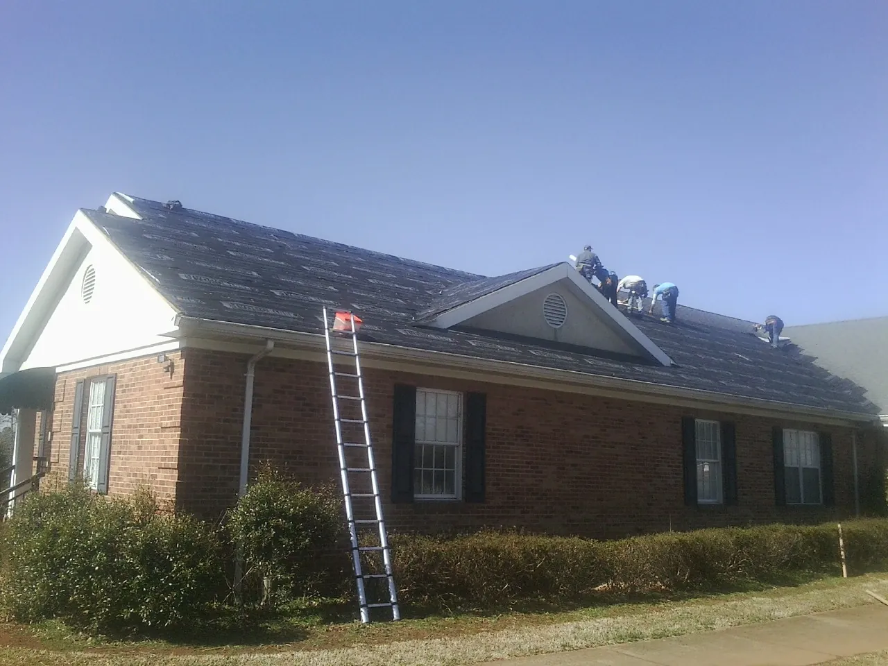 Crew tearing shingles off a brick ranch roof with a ladder set — Metal Roof Repair work by our crew in Fox River Grove