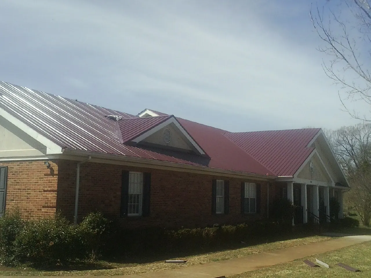 Red metal roof with gabled entries on a long brick building, from a Hail Damage Roof Repair job in Fox River Grove
