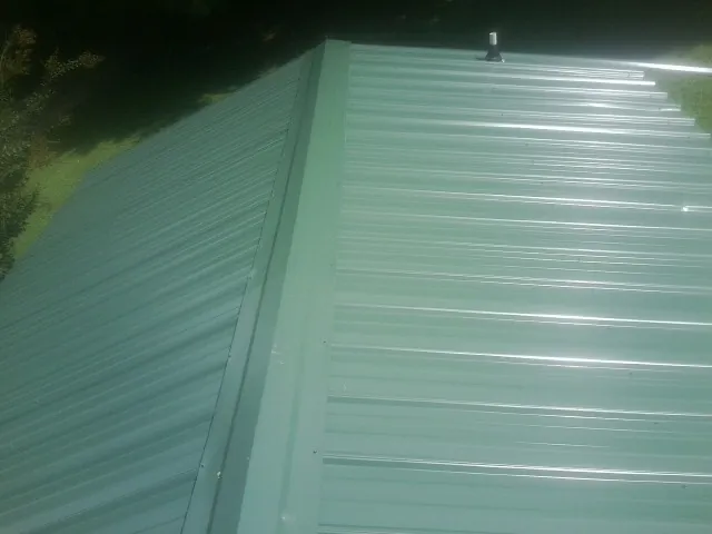 New green metal panels meeting at the ridge of a roof — Flat Roof Repair work by our crew in Fox River Grove