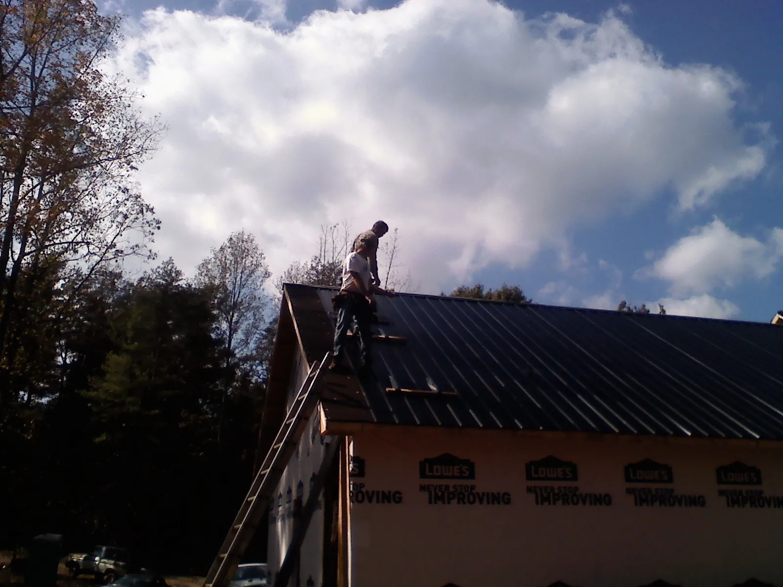 Roofer fastening dark metal panels high against a cloudy sky, from a Roof Inspection job in Fox River Grove