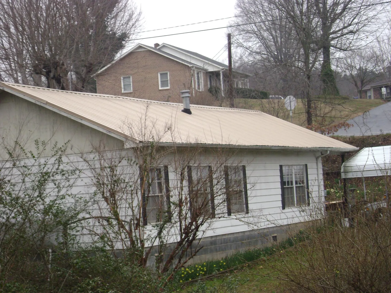 Tan metal roof on a white sided house set into a hillside — Commercial Roofing by Roofing Brothers in Fox River Grove